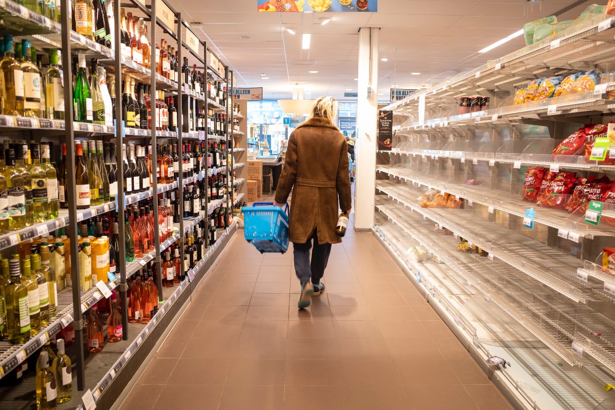 reduce food waste ukds blog woman walking down the middle of a supermarket aisle carrying a blue basket. Shelves are full, we cannot see her face